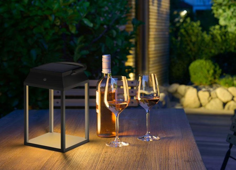 Die Solar-Akkuleuchte p.089 von prediger.base beleuchtet den Tisch auf einer Terrasse, darauf eine Weinflasche und zwei Gläser. (Foto: Prediger Lichtberater)