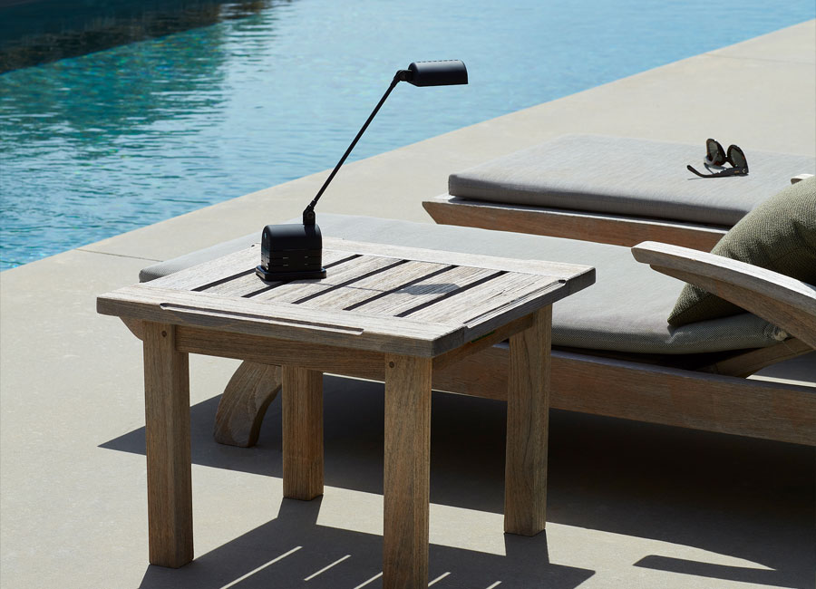 Die Akku-Tischleuchte Daphinette LED Portatile steht an einem Pool auf einem kleinen Tisch neben einer Liege. (Foto: Lumina) 