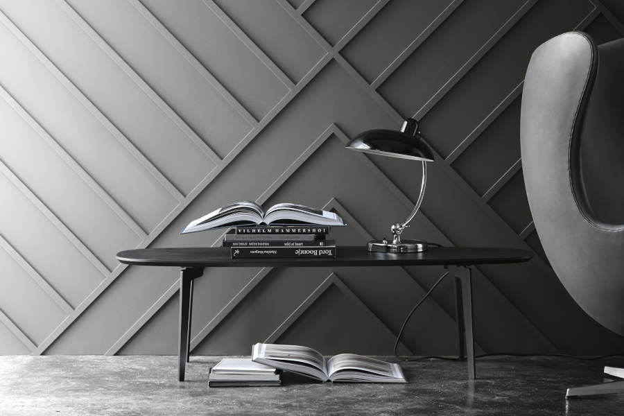 Die Tischleuchte KAISER idell 6631-T Luxus in Schwarz steht auf einem Beistelltisch neben einem Sessel und beleuchtet ein aufgeschlagenes Buch. (Foto: Fritz Hansen) 