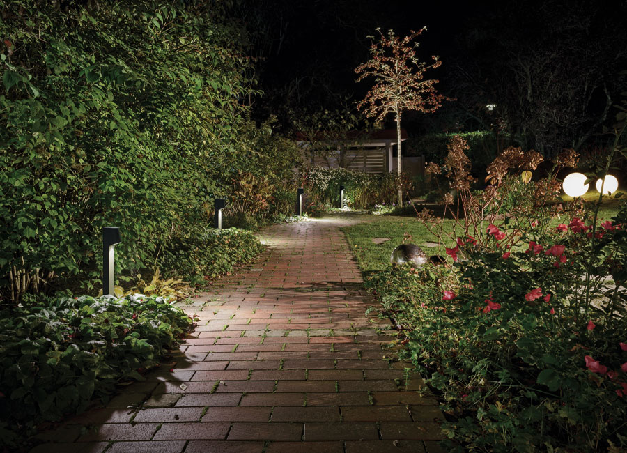 Ein Garten bei Nacht mit Wegebeleuchtung durch Pollerleuchten und zwei kugelförmigen Lichtobjekten als Blickfang.