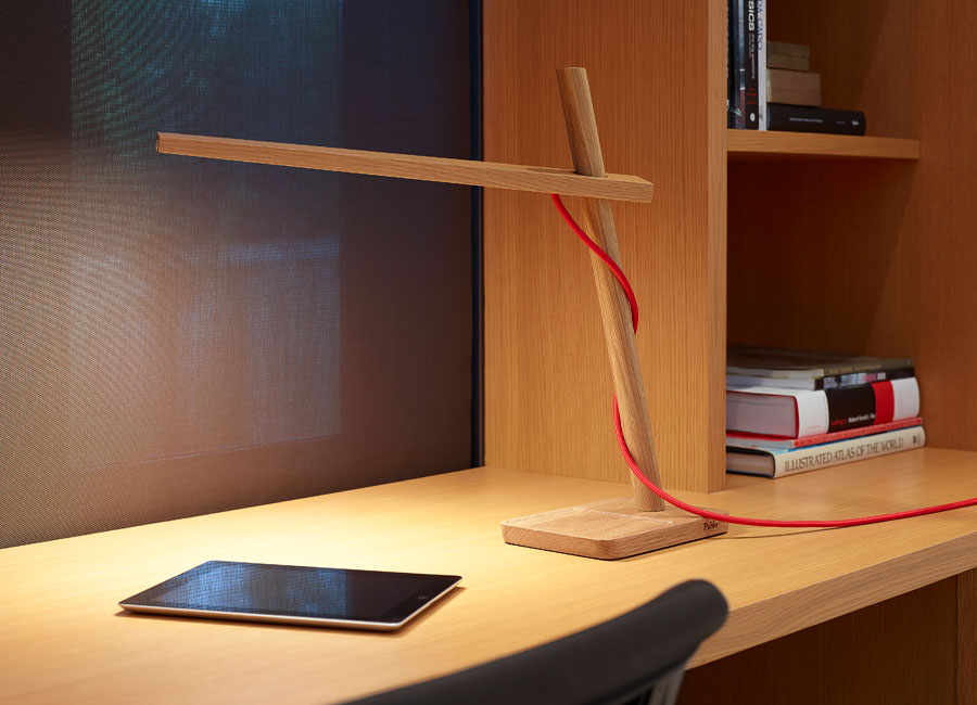 Eine minimalistisch designte Tischleuchte Clamp Mini von Pablo Designs in Eiche mit rotem Kabel steht auf einem Schreibtisch und beleuchtet ein Tablet. (Foto: Pablo Designs)