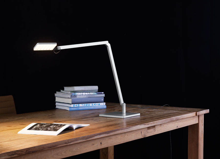 Eine Roxxane Home LED Tischleuchte steht auf einem hölzernen Schreibtisch und beleuchtet ein Buch. (Foto: Nimbus)