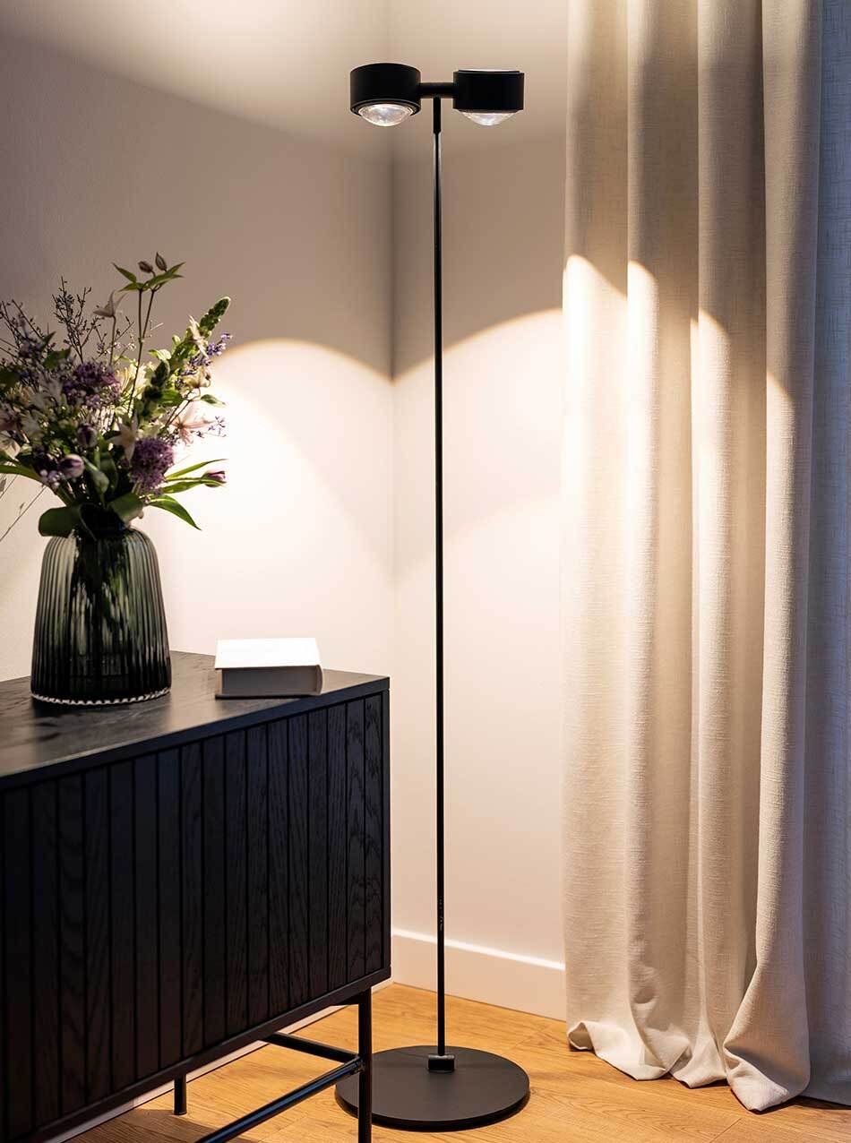 Modernes Schlafzimmer mit einer s.200 Stehleuchte von prediger.select in Schwarz, die neben einer schwarzen Kommode mit einem Blumenstrauß steht.