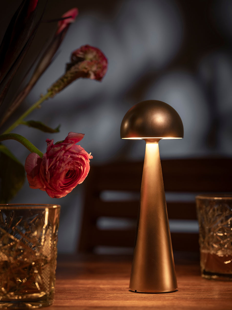Terrasse in der Abenddämmerung mit pilzförmiger Akku-Tischleuchte von prediger.base in rose gold, die auf einem Esstisch steht.