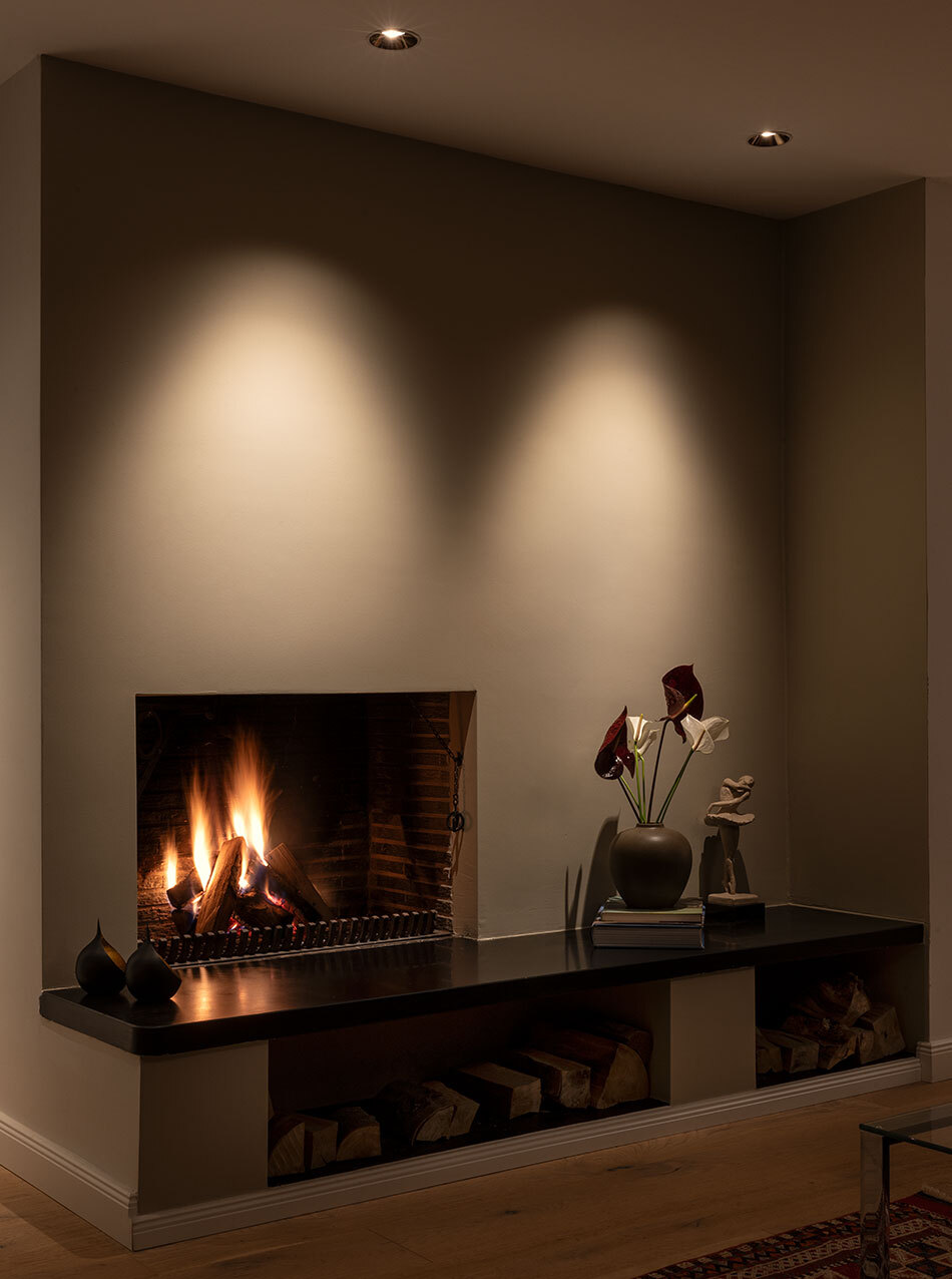 Wohnzimmer mit brennendem Feuer in einem offenen Kamin. An der Decke oberhalb des Kamins sind zwei Downlights von prediger.base.