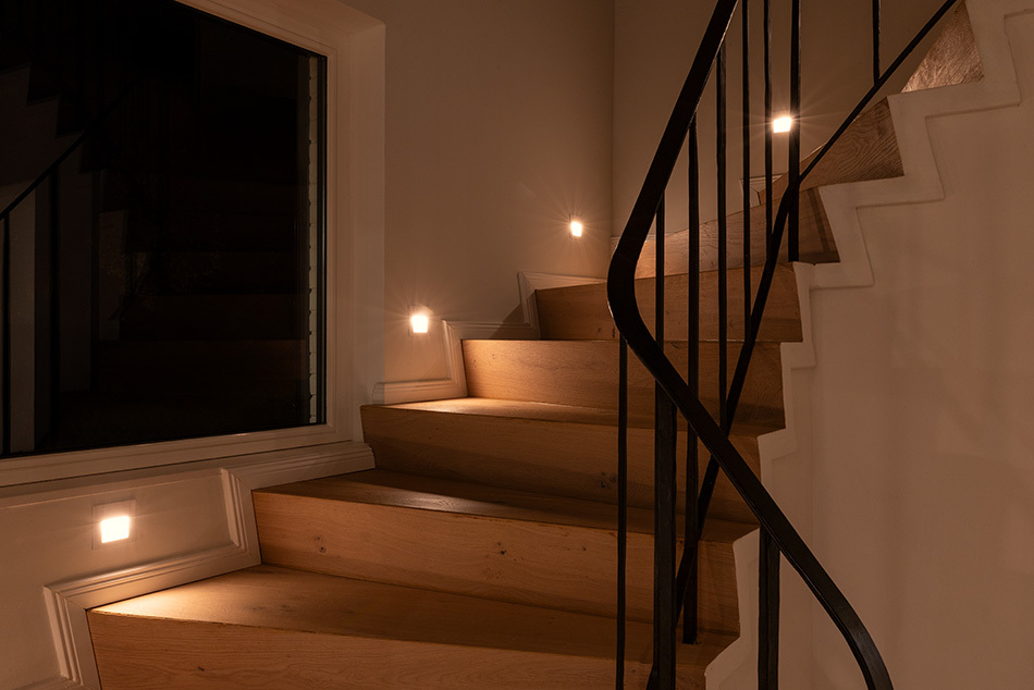 Holztreppe mit mehreren p.076 Einbau-Wandleuchten von prediger.base, die für Sicherheit sorgen und die Treppenstufen beleuchten.