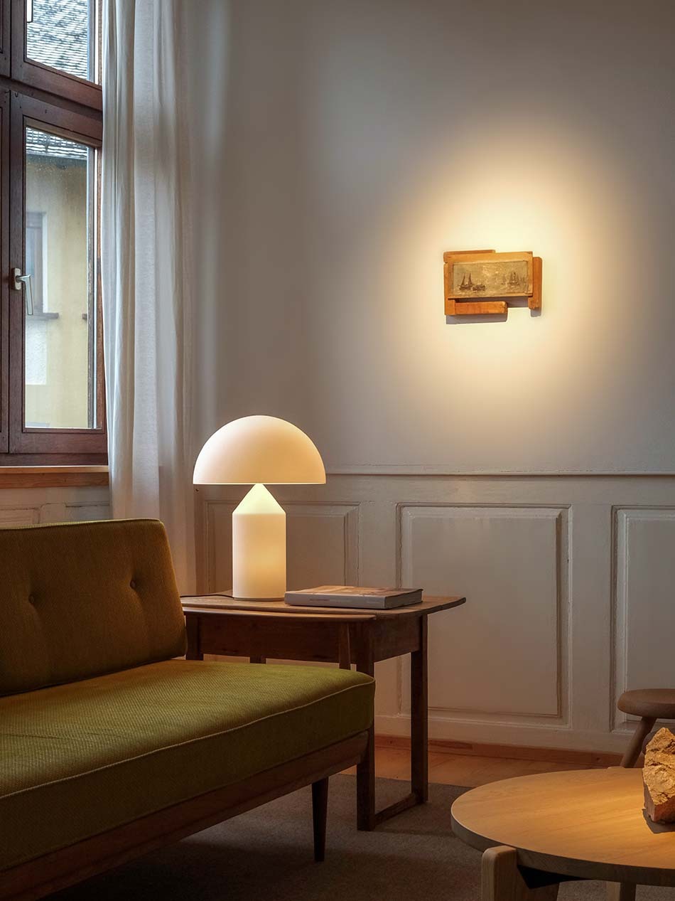 Minimalistisches Wohnzimmer mit einem dunkelgrünen Sofa und einer Atollo Stehleuchte in Weiß von Oluce, die auf einem Holz-Beistelltisch steht.