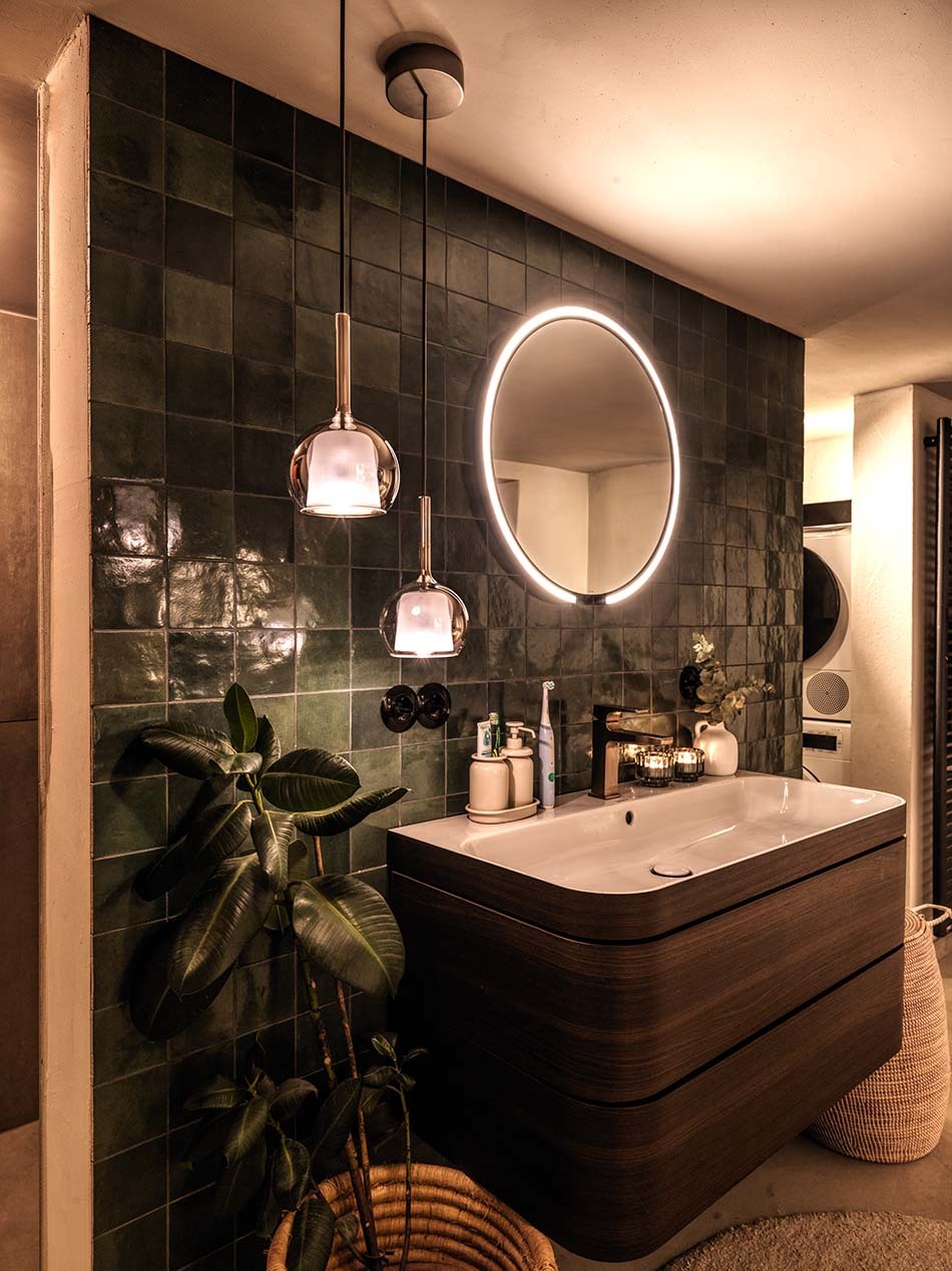 Modernes Badezimmer mit einem beleuchteten Mito sfera Wide Spiegel von Occhio sowei zwei Glo Pendelleuchten von Penta in unterschiedlichen Größen, die neben dem Waschbecken hängen.