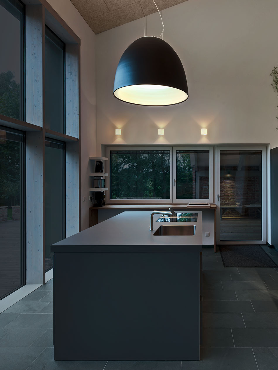 Moderne schlichte Küche mit einer großen Kochinsel, über der eine Nur Pendelleuchte in schwarz von Artemide hängt.