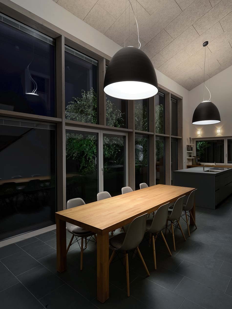 Großer Essbereich mit einem langen Holzesstisch, über dem eine Nur Halo Pendelleuchte in schwarz von Artemide hängt. Auch über der Kücheninsel hängt eine weitere Nur Halo Pendelleuchte.