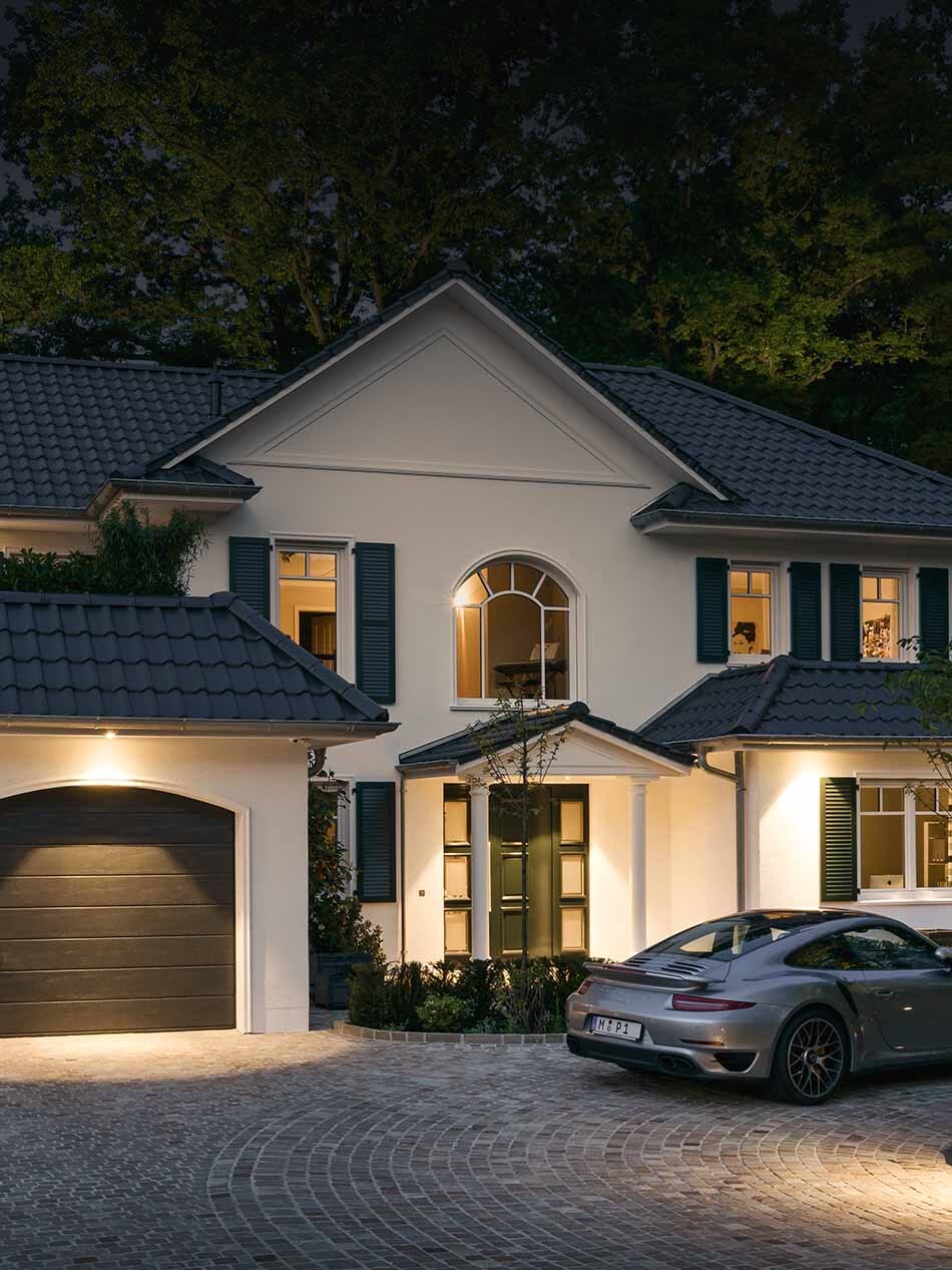 Außenaufnahme bei Abenddämmerung einer Stadtvilla. Die Fassade wird durch mehrere Decken-Einbauleuchten von Bega beleuchtet.
