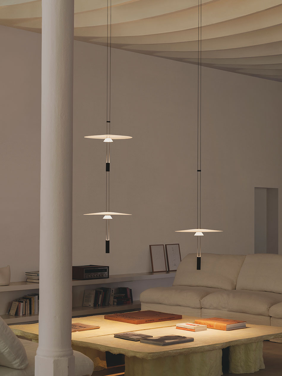 Wohnzimmer mit zwei Flamingo Pendelleuchten, die einen großen tiefen Couchtisch, auf dem viele Magazine liegen, beleuchten. (Foto: Vibia)