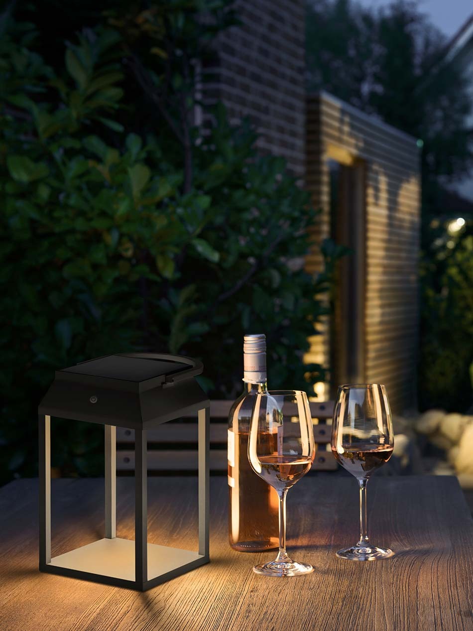 Terrasse mit einem großen Esstisch und einer schwarzen p.089 Solar-Akkuleuchte von prediger.base. Neben der Leuchte stehen zwei gefüllte Weingläser sowie eine Weinflasche.
