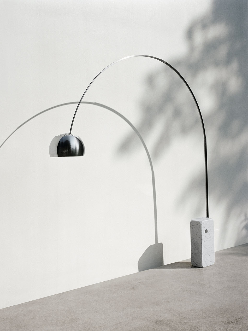 Terrasse bei Tageslicht mit Arco Bogenleuchte, die vor einer weißen Wand mit Schattenmustern steht. (Bild: Flos)