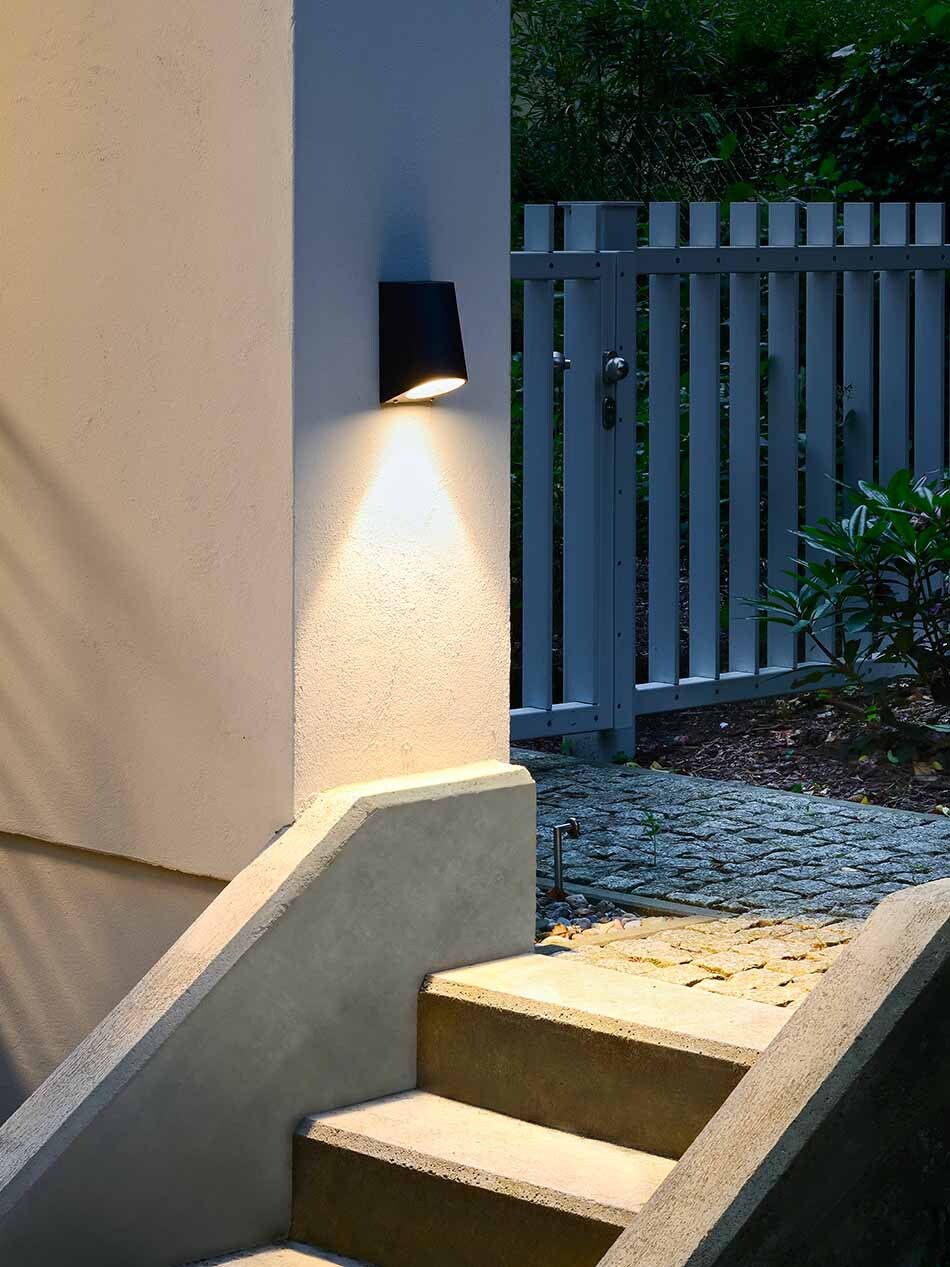 Das Bild zeigt eine schwarze halbrunde Wandleuchte von Bega, die eine kleine Treppe beleuchtet und für Sicherheit sorgt.