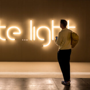Ein Besucher steht vor dem beleuchteten Logo der Ausstellung "Sate...light", die 2023 im Rahmen der Euroluce stattgefunden hat.