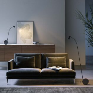 Eine Stehleuchte und eine Tischleuchte der Chiocciola-Familie des Herstellers Lumen Center beleuchten eine Wohnzimmer-Szene mit Couch und Sideboard. (Foto: Lumen Center)