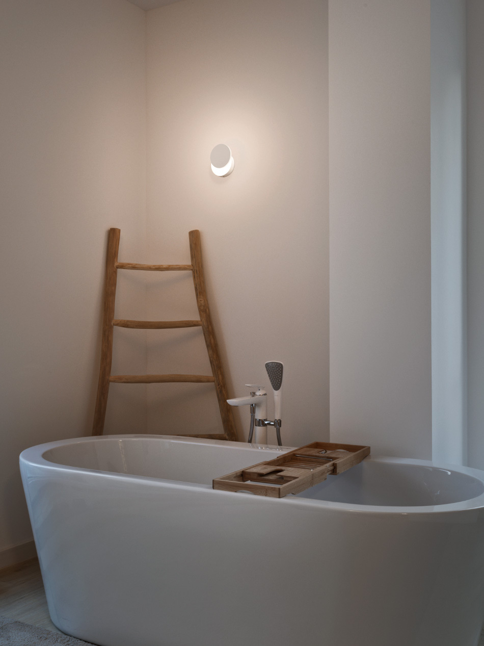 Badezimmer mit freistehender Badewanne und einer p.017 Wandleuchte von prediger.base in Weiß.