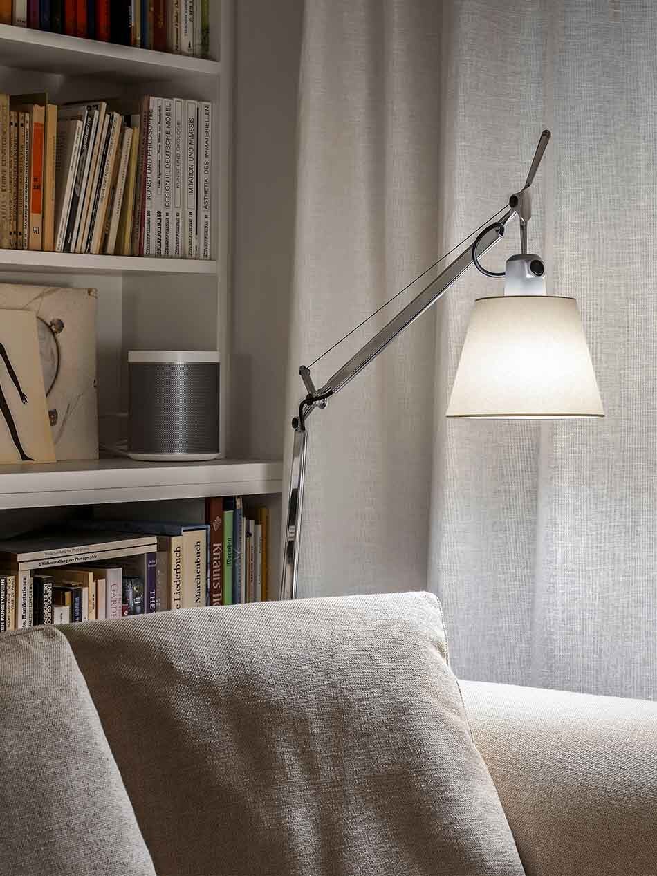 Wohnzimmer mit einer Tolomeo Basculante Lettura Standleuchte von Artemide, die zwischen einem Bücherregal und einem Sofa steht.