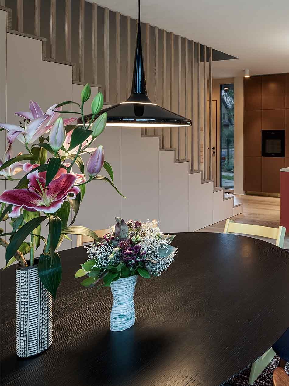Über einem ovalen, schwarzen Esstisch hängt eine schwarze Juicy Pendelleuchte von Fritz Hansen. Im Hintergrund ist der Kochbereich, der Eingang und die Treppe zu sehen.