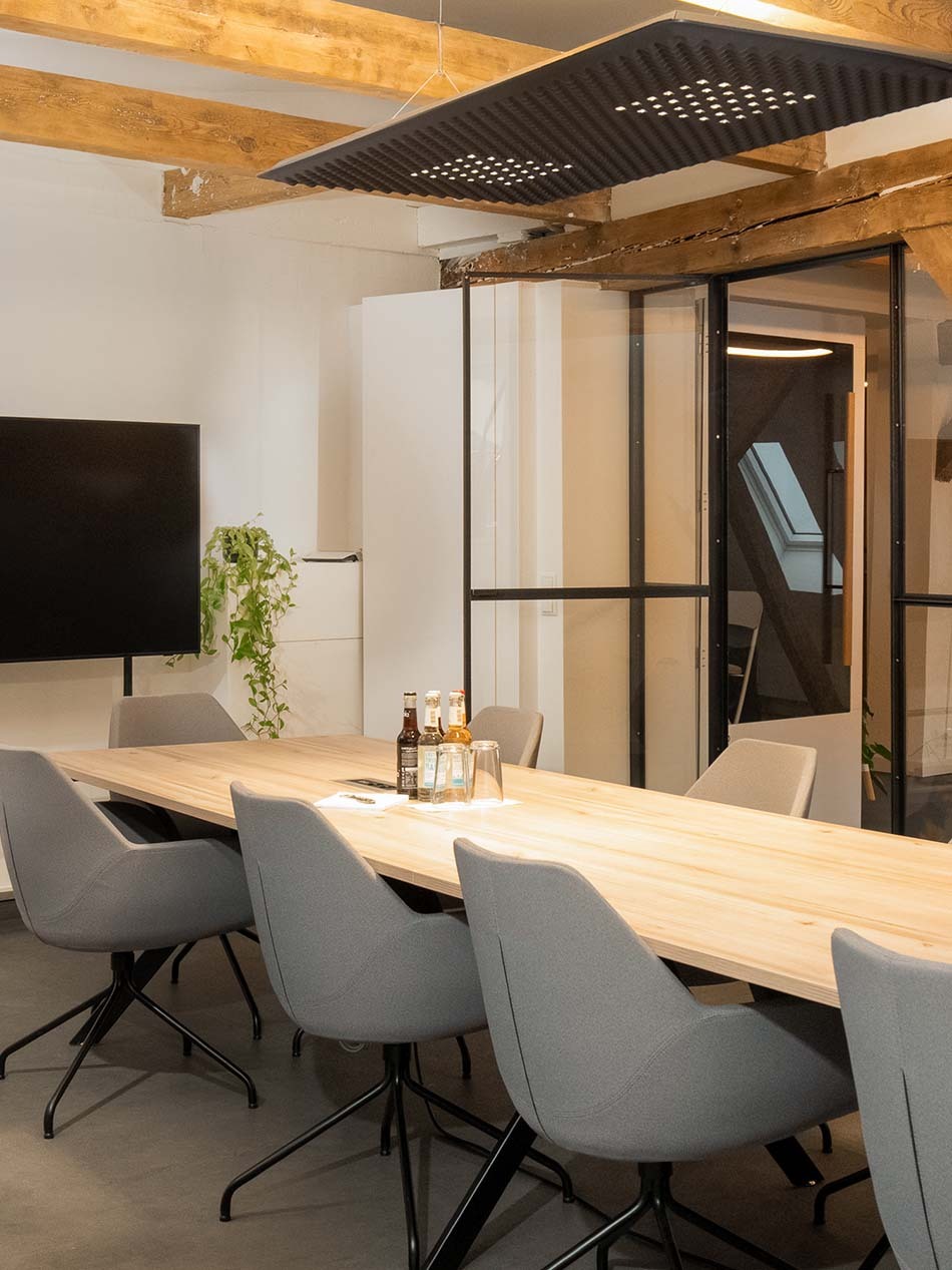 Moderner Konferenzraum in einem Hamburger Büro mit einer Eggboard Pendelleuchte von Artemide. Die Pendelleuchte hängt über einem großen Meetingstisch, an dem mehrere graue Polsterstühle stehen.