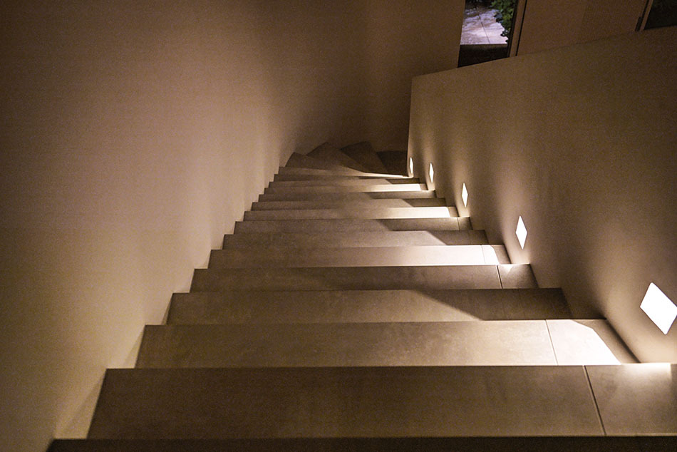 Moderne breite Treppe mit mehreren p.108 Wandleuchten von prediger.base, die die Treppenstufen beleuchten und für Sicherheit sorgen.