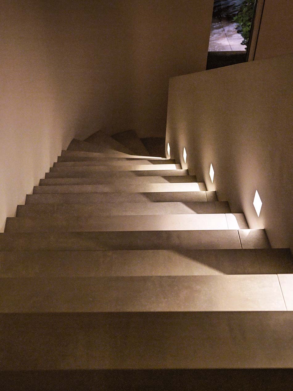 Moderne breite Treppe mit mehreren p.108 Wandleuchten von prediger.base, die die Treppenstufen beleuchten und für Sicherheit sorgen.