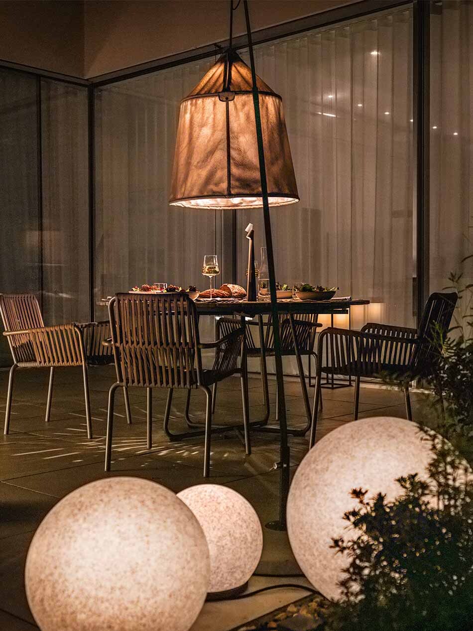 Neben einer Terrasse stehen drei p.111 Kugelleuchten von prediger.base in unterschiedlichen Größen. Die Terrasse wird durch eine große Standleuchte von Marset beleuchtet. Auf dem Tisch steht eine Africa Tisch- und Akkuleuchte von Vibia.