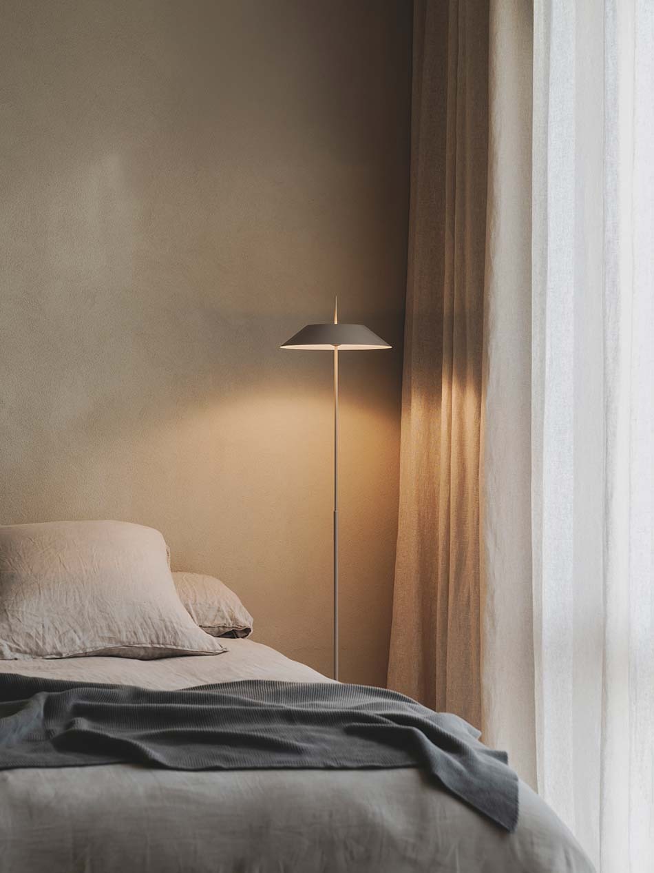 Schlichtes Schlafzimmer mit Mayfair Standleuchte von Vibia. Die Stehleuchte steht zwischen einem Bett und einem bodentiefen Fenster. (Foto: Vibia)