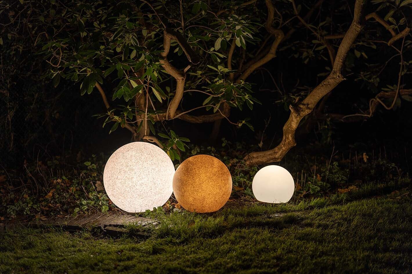Aufnahme eines Garten bei Nacht mit drei Kugelleuchten p.111 von prediger.base in drei unterschiedlichen Farben und Größen. Die leuchten geben diffuses Licht ab und beleuchten die Vegetation im Hintergrund.