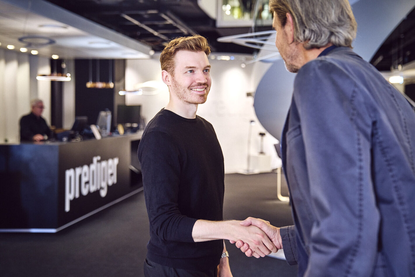 Ein junger Lichtberater lächelt und spricht mit einem Kunden im Prediger Showroom. Im Hintergrund ist der Empfangsbereich von Prediger zu sehen. (Foto: Johannes Arlt)