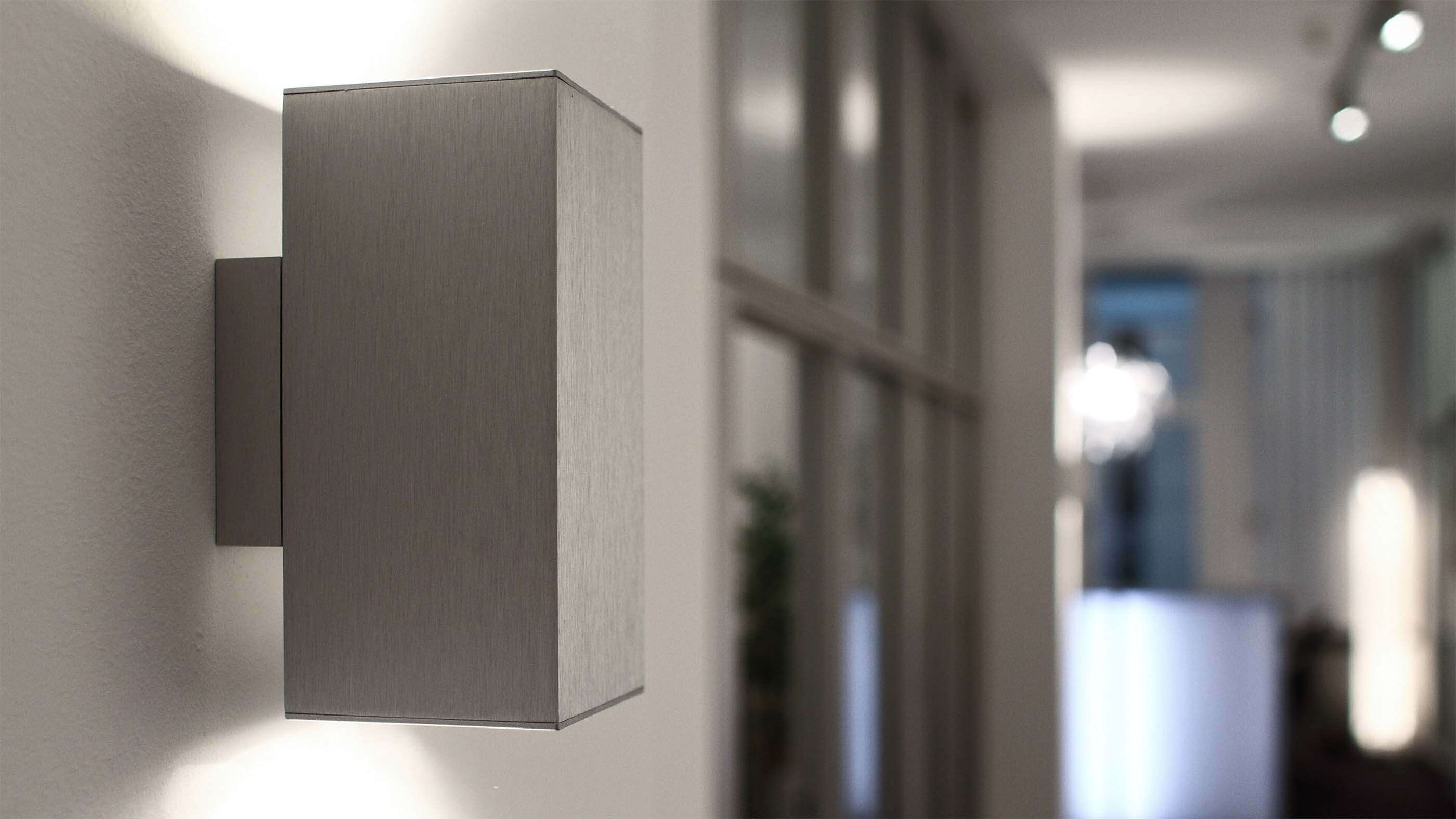 Nahaufnahme einer beidseitig strahlenden Wandleuchte von Bega in Silber in einem Flur.