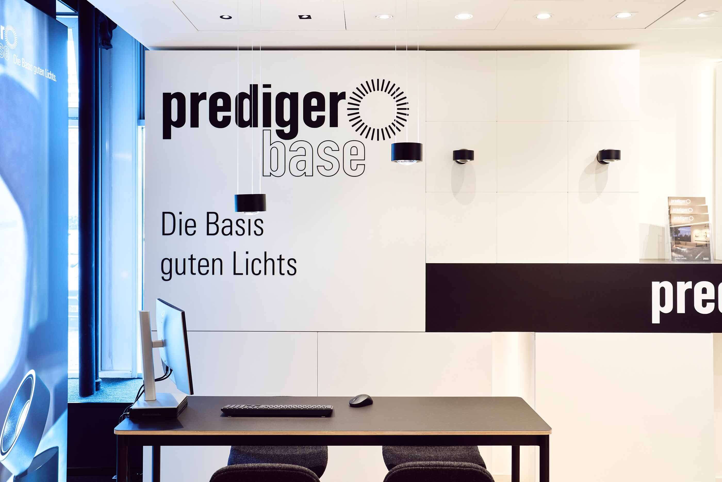 Blick in unseren Showroom: Am POS von prediger.base werden die Leuchten der Marke präsentiert. Vor dem POS steht ein Schreibtisch mit einem PC und einer Tastatur.
