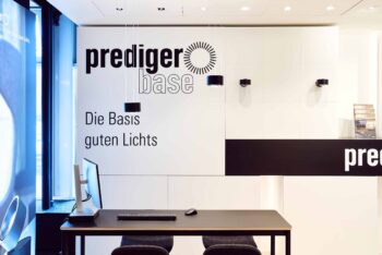 Blick in unseren Showroom: Am POS von prediger.base werden die Leuchten der Marke präsentiert. Vor dem POS steht ein Schreibtisch mit einem PC und einer Tastatur.