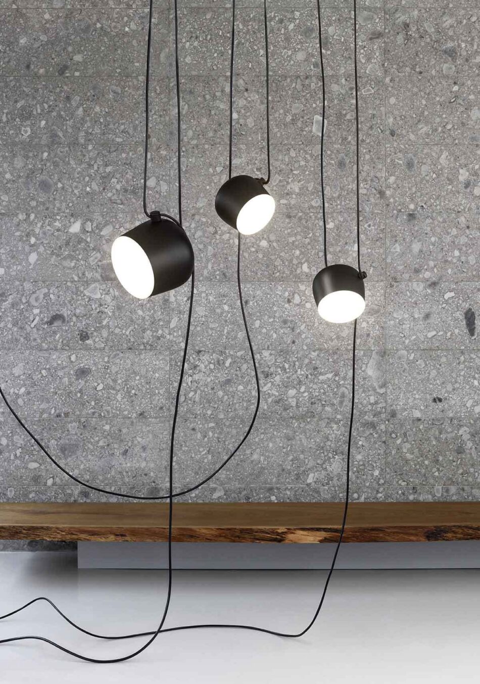 Drei moderne Aim Pendelleuchten in Schwarz von Flos hängen in einem Raum von der Decke. (Bild: Flos)