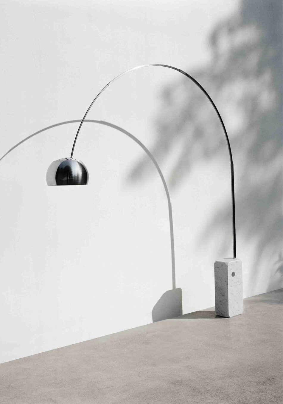 Terrasse mit Standleuchte Arco von Flos in Silber, die an einer weißen Wand mit Schattenmuster steht. (Foto: Flos)