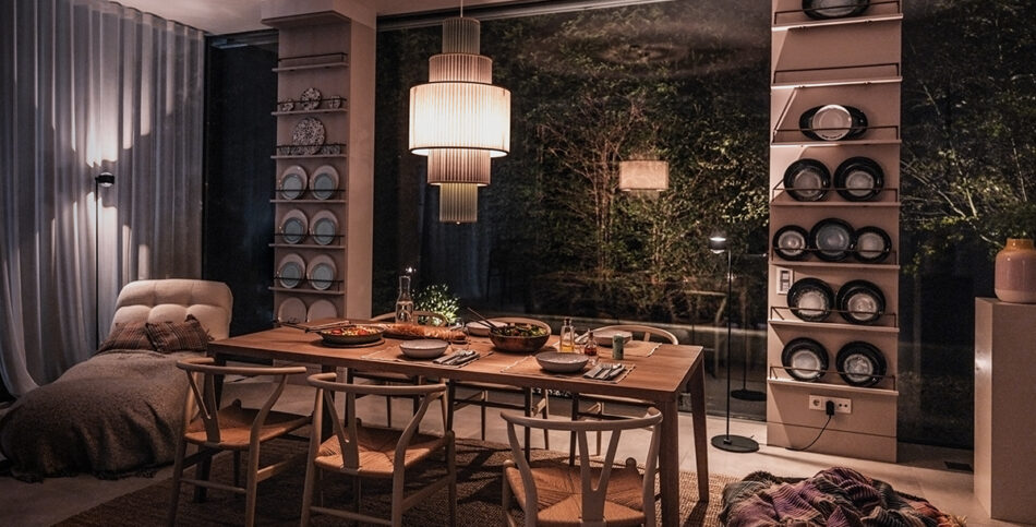 Modernes Esszimmer mit gedecktem Esstisch unter einer grünen Pendelleuchte Plivello von Le Klint. Im Hintergrund stehen zwei schwarze s.200 Stehleuchten von prediger.select. Der Raum ist stilvoll und modern eingerichtet.