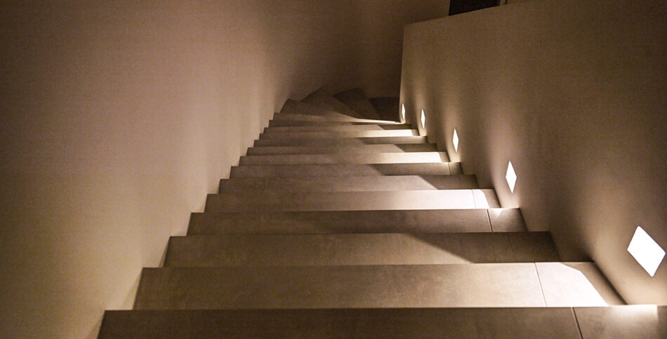 Moderne breite Treppe mit mehreren p.108 Wandleuchten von prediger.base, die die Treppenstufen beleuchten und für Sicherheit sorgen.