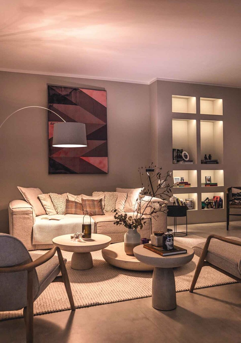 Modernes Wohnzimmer einer Villa mit unterschiedlichen Lichtquellen. Neben dem Sofa steht eine Bogenleuchte Twiggy von Foscarini. Die Wandregale werden von Lichtleisten von prediger.base beleuchtet. Das Wohnzimmer ist gemütlich eingerichtet.