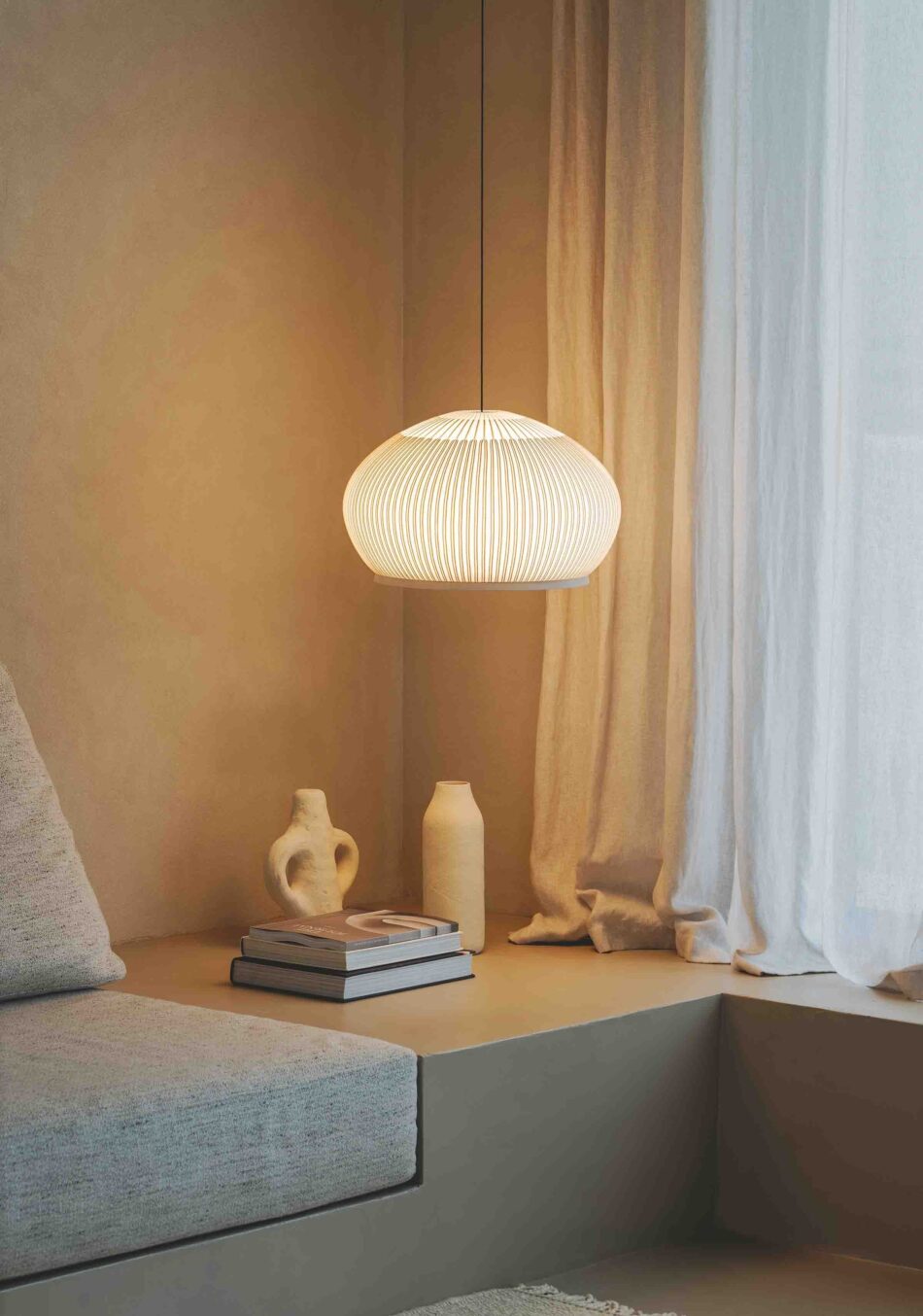 Wohnzimmer mit hellen beigen Tönen und einer Pendelleuchte Knit, die eine Ecke mit dekorativen Elementen beleuchtet. (Foto: Vibia)