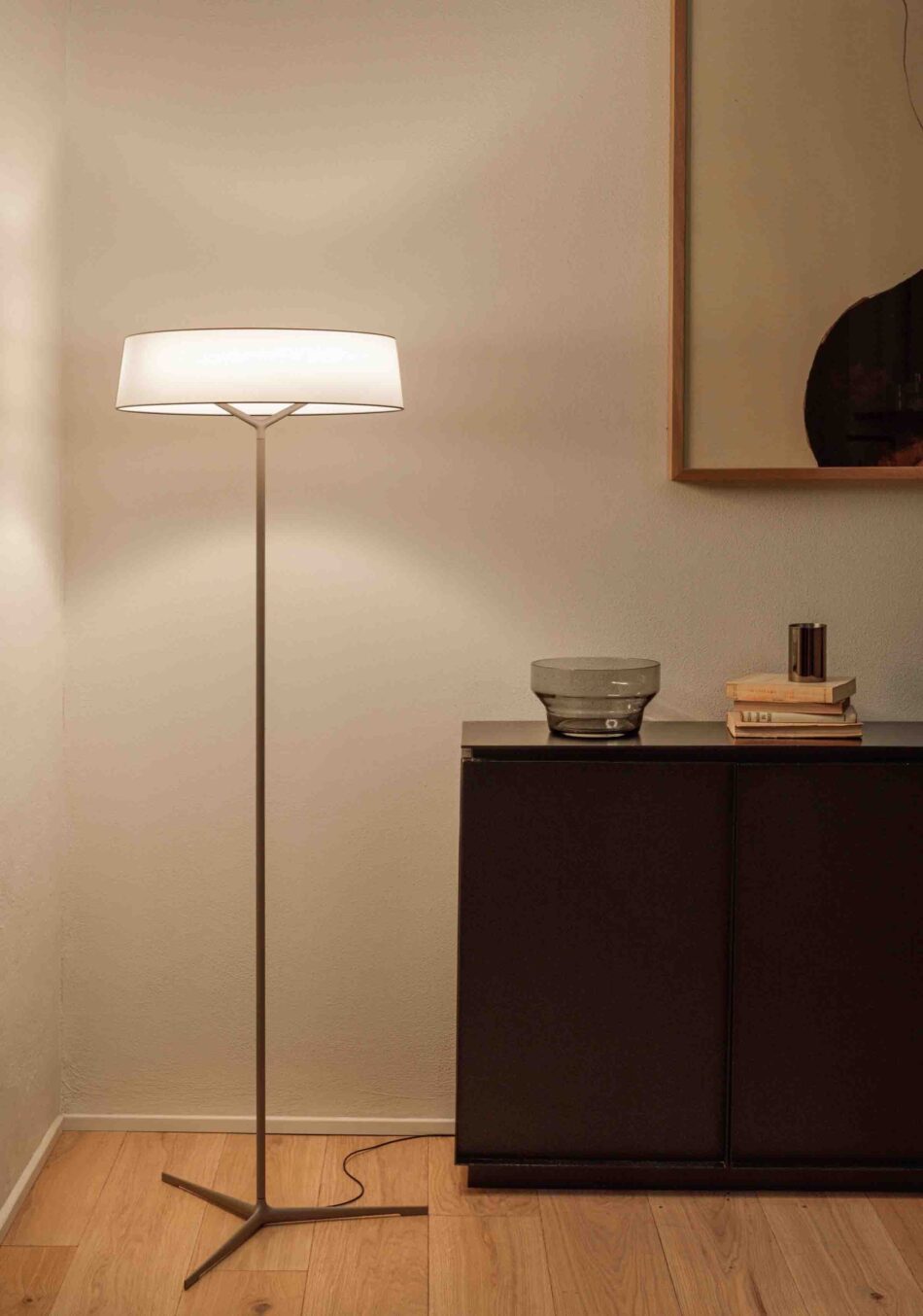 Schlafzimmer mit Dama Standleuchte von Vibia, die neben einer Holzkommode steht und Licht nach oben und unten abstrahlt. (Foto: Vibia)