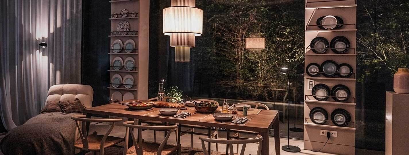 Modernes Esszimmer mit gedecktem Esstisch unter einer grünen Pendelleuchte Plivello von Le Klint. Im Hintergrund stehen zwei schwarze s.200 Stehleuchten von prediger.select. Der Raum ist stilvoll und modern eingerichtet.