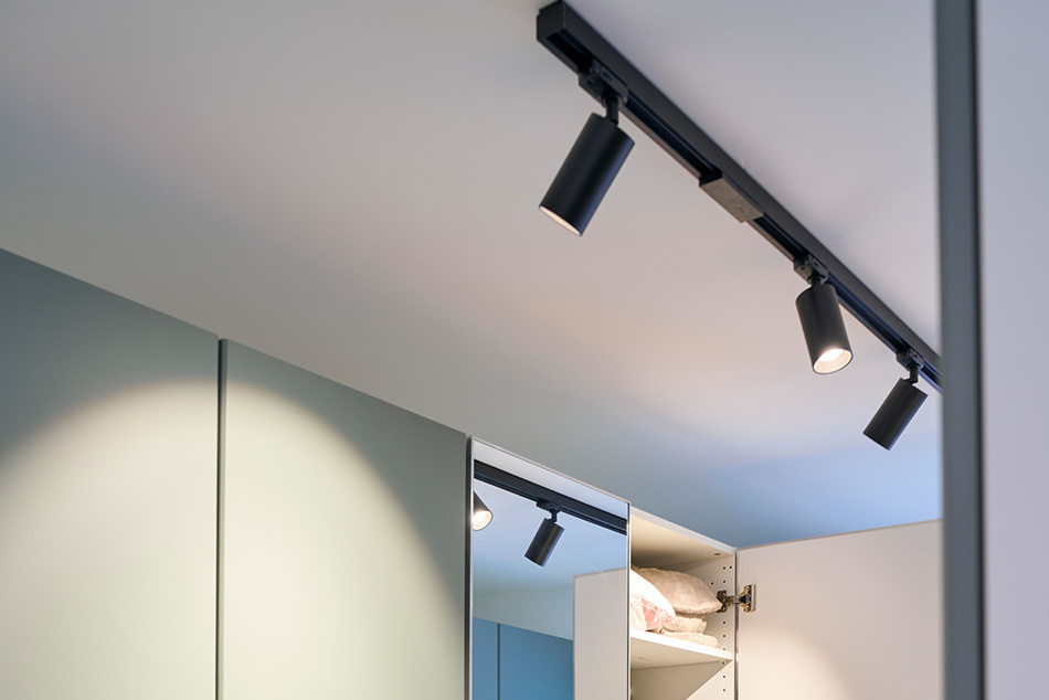 Ankleidezimmer mit schwarzen p.035 Schienenstrahlern von prediger.base, die einen grünen Kleiderschrank beleuchten.