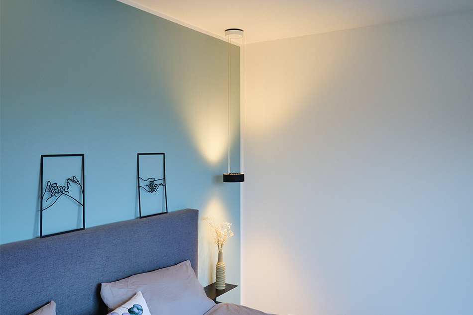 Schlafzimmer mit einer c.Pace Pendelleuchte von CHRISTOPH, die als Nachttischleuchte dient und Licht nach oben und unten strahlt.
