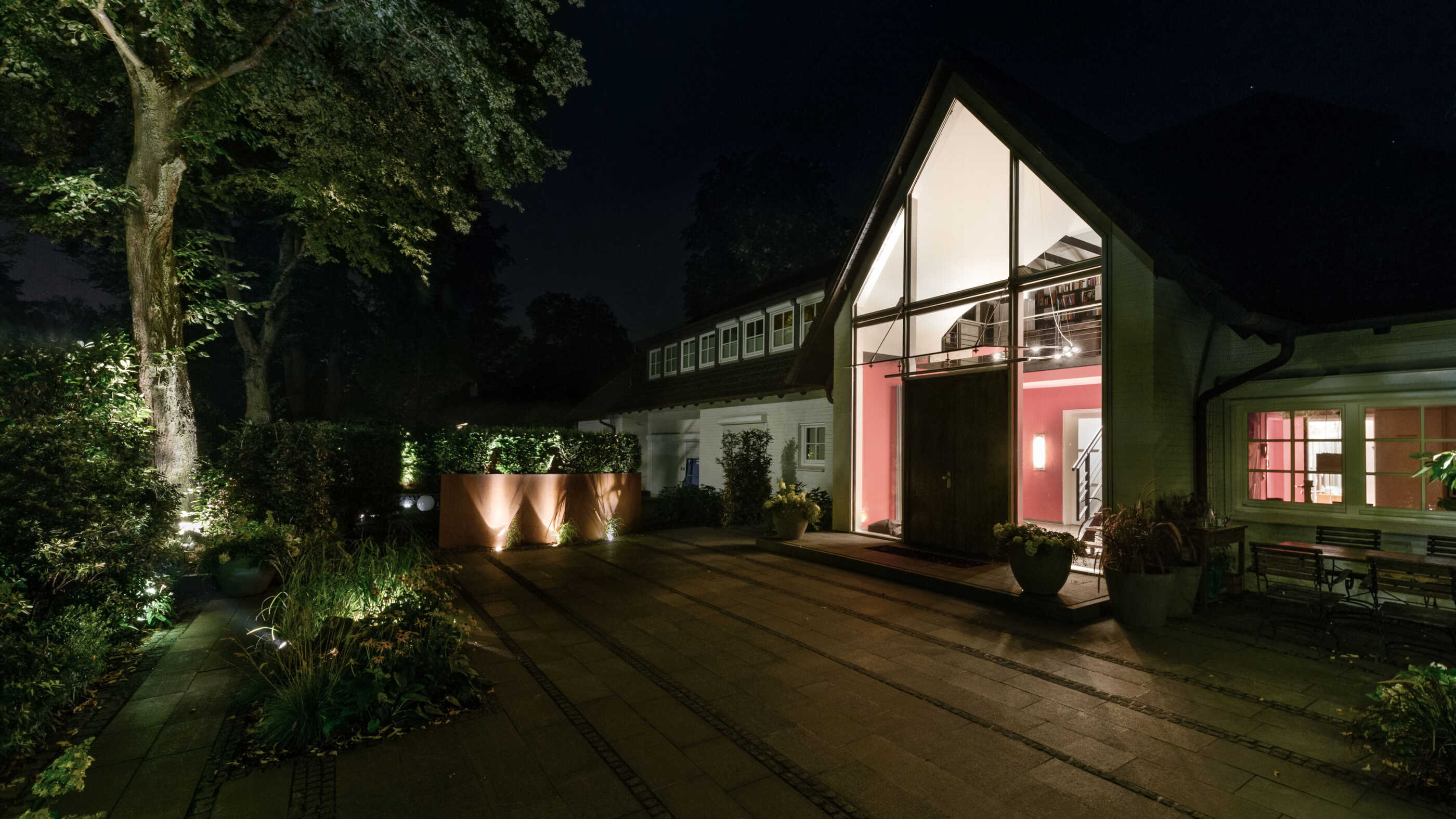 Eine Terrasse bei Nacht: Ein ovales Hochbeet aus Metall wird von drei Bodenstrahlern indirekt angestrahlt. (Foto. Prediger Lichtberater)