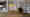 Das Wohnzimmer in einer Wohnung in Hamburg Altona: Ein Bücherregal nimmt die gesamte rechte Seite ein, davor stehen ein Sessel, eine Leseleuchte und ein kleiner Tisch. Links ist eine offene Küche zu sehen. (Foto: Prediger Lichtberater) imageThumbnailAlt