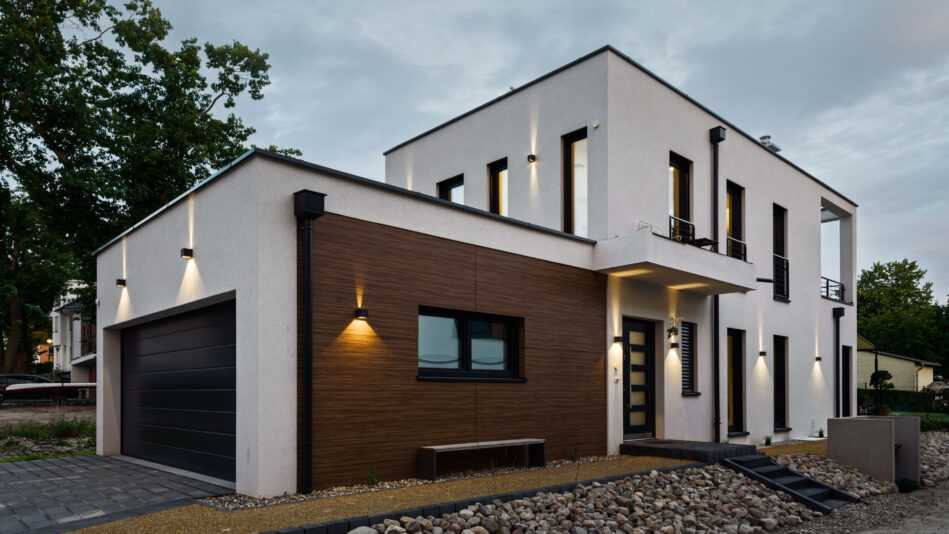 Ein modernes, zweigeschossiges Wohnhaus mit angeschlossener Garage. Zweiseitig strahlende Wandleuchten beleuchten die Fassade. (Foto: Prediger Lichtberater)