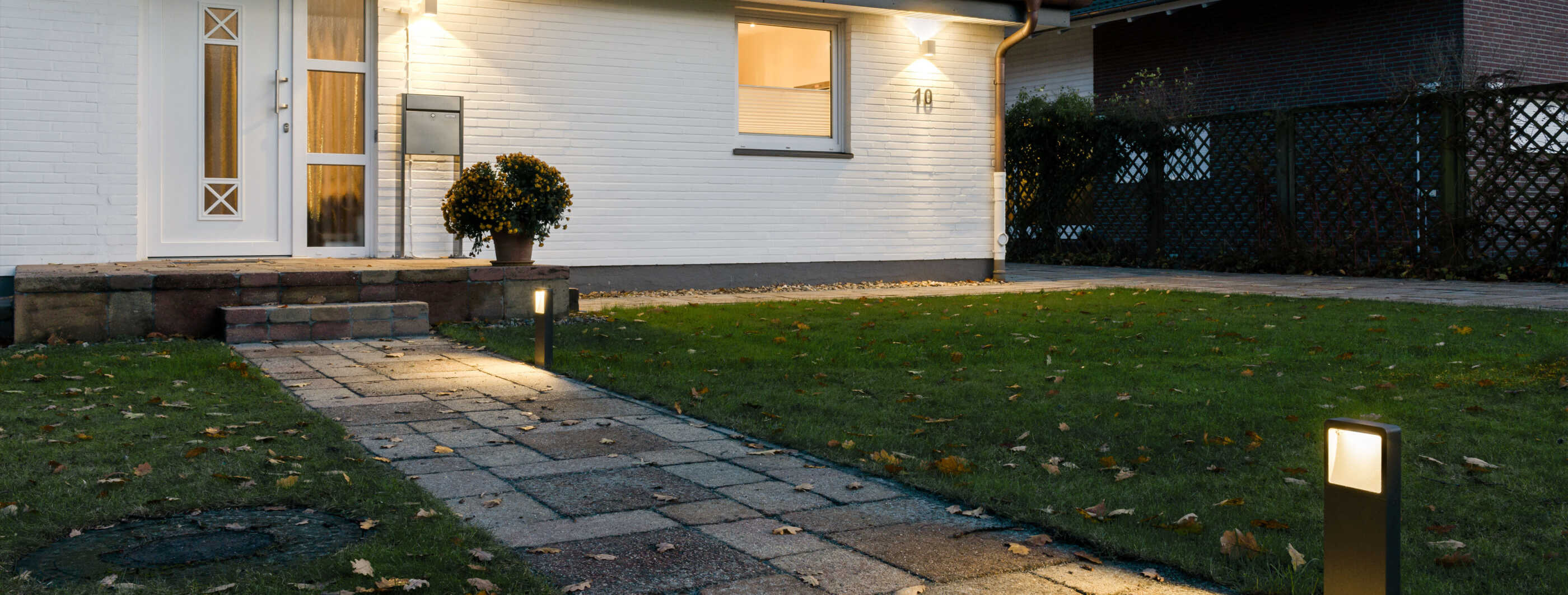 Der Zuweg zu einem Einfamilienhaus durch den Vorgarten: Wandleuchten beleuchten die Fassade, Sockelleuchten werfen Licht auf den Weg. (Foto: Prediger Lichtberater)