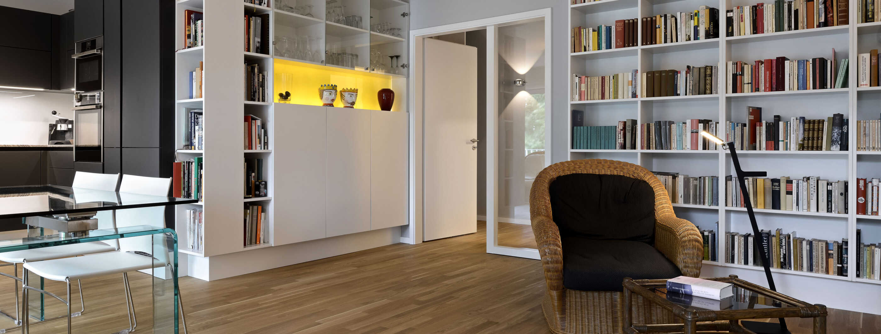 Das Wohnzimmer in einer Wohnung in Hamburg Altona: Ein Bücherregal nimmt die gesamte rechte Seite ein, davor stehen ein Sessel, eine Leseleuchte und ein kleiner Tisch. Links ist eine offene Küche zu sehen. (Foto: Prediger Lichtberater)