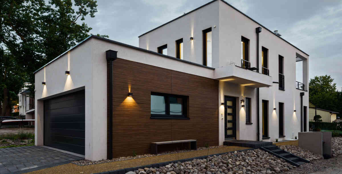 Ein modernes, zweigeschossiges Wohnhaus mit angeschlossener Garage. Zweiseitig strahlende Wandleuchten beleuchten die Fassade. (Foto: Prediger Lichtberater)